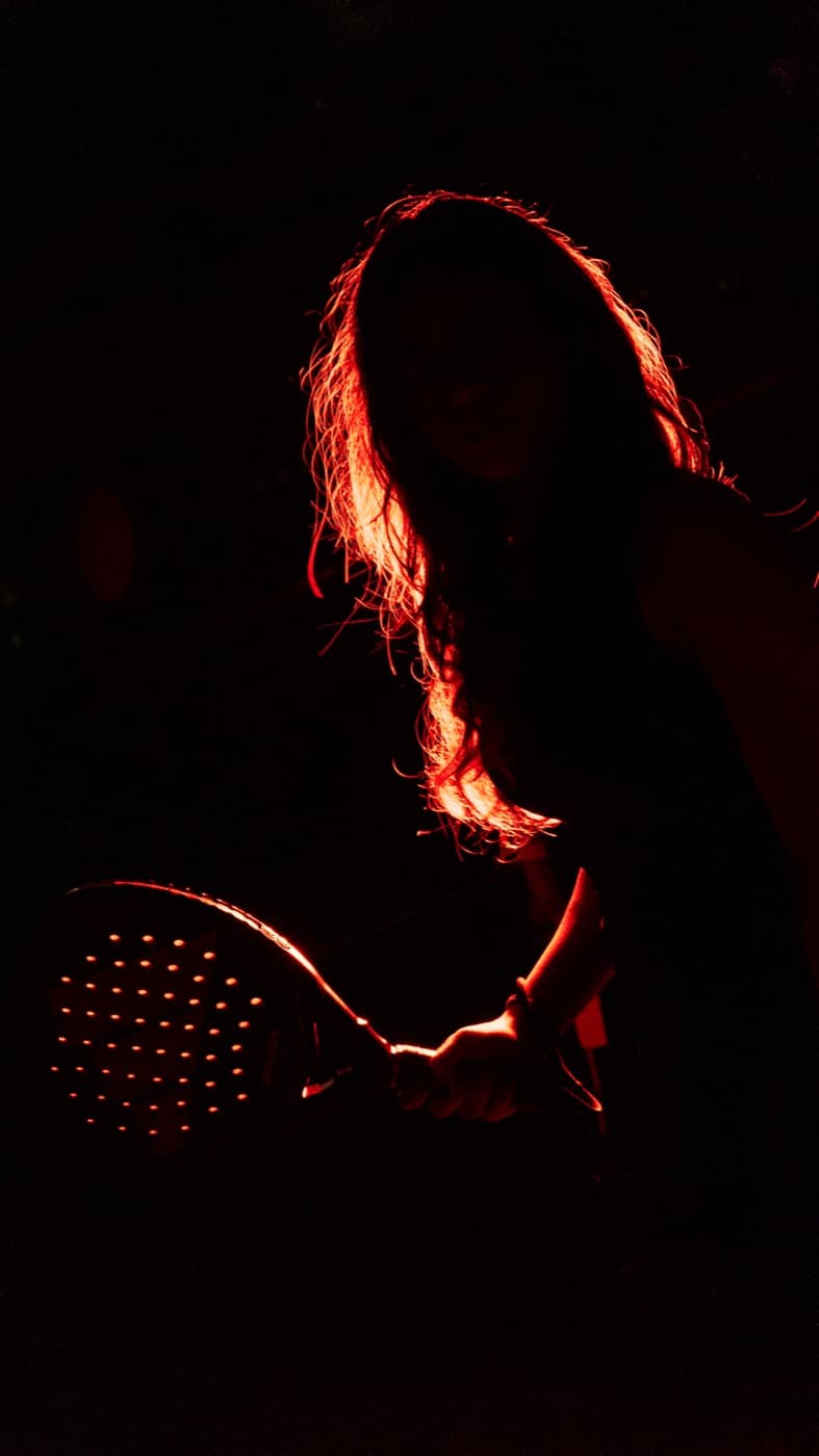 Backlit padel player holding a racket in red light
