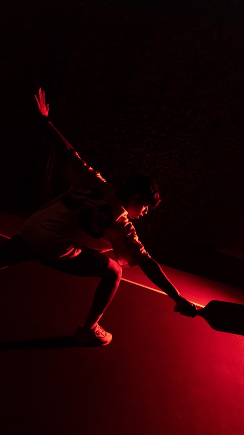 Pickleball player lunging low for a shot under red light